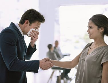Man sneezing into hand ill and shaking hands with woman