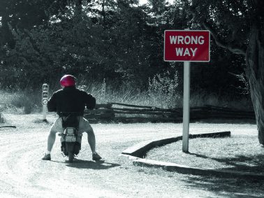 Man on scooter with wrong way sign.